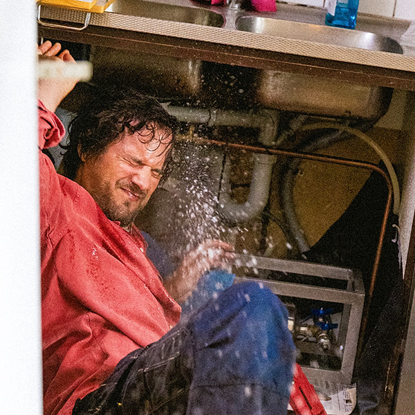 Man som försöker stoppa vattenläcka under vasken.