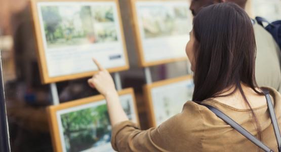 Ett par tittar på mäklarobjekt i ett skyltfönster.