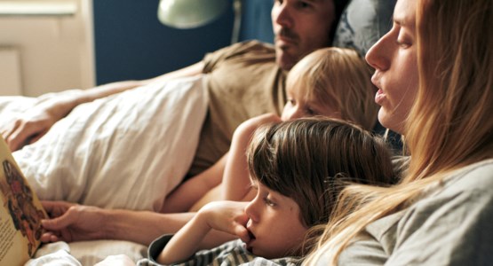 Familj ligger i sängen och läser en bok.