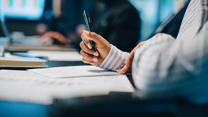 En kvinna sitter med en penna i handen, på väg att skriva något i ett anteckningsblock.