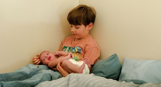 Pojke sitter i säng med bebis i knät.