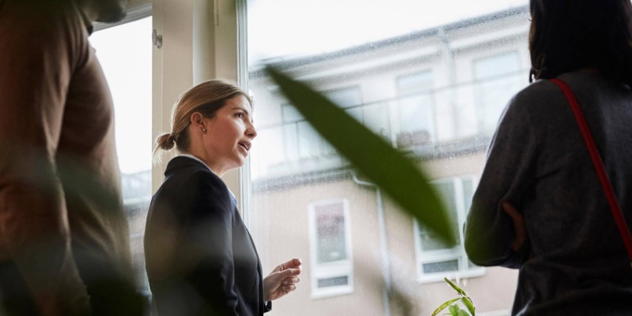 En kvinna står vid ett lägenhetsfönster och pratar med en annan person med ryggen mot kameran.