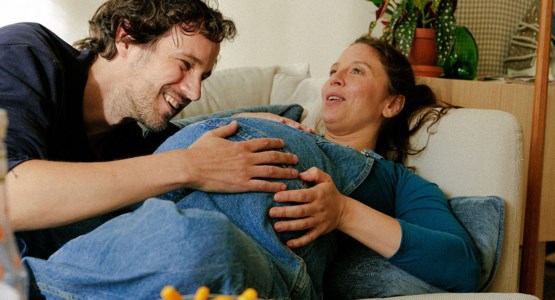 Höggravid kvinna ligger i soffa. Man klappar hennes mage.